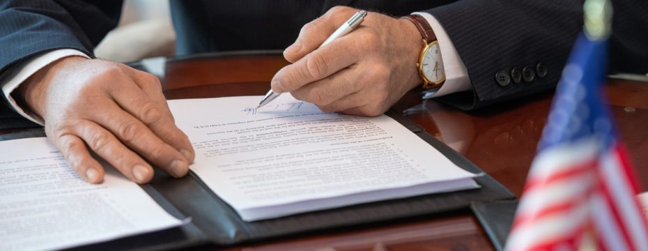 someone signing a bill with an American flag in the foreground